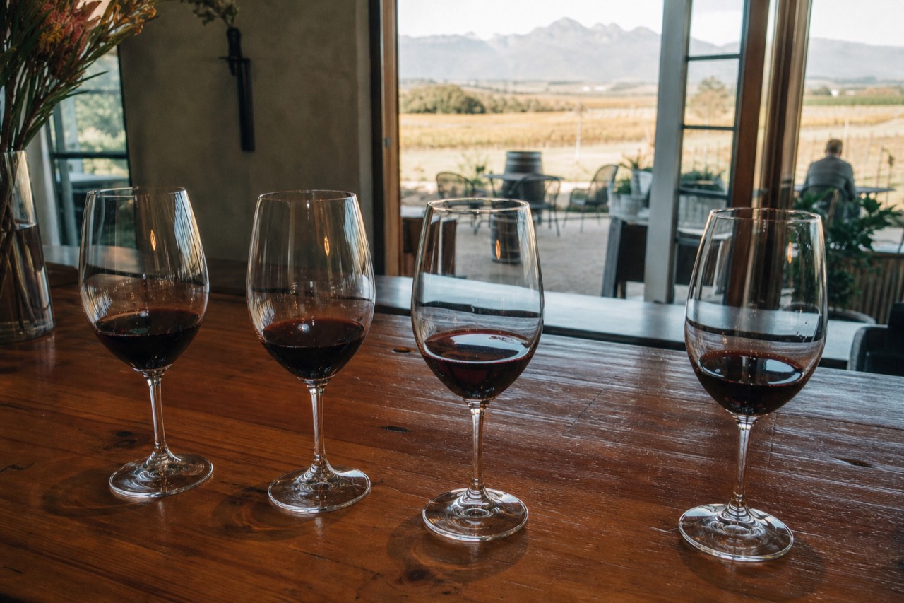 A tasting flight of red wine glasses on a wooden cellar counter, no text, no logos, no people