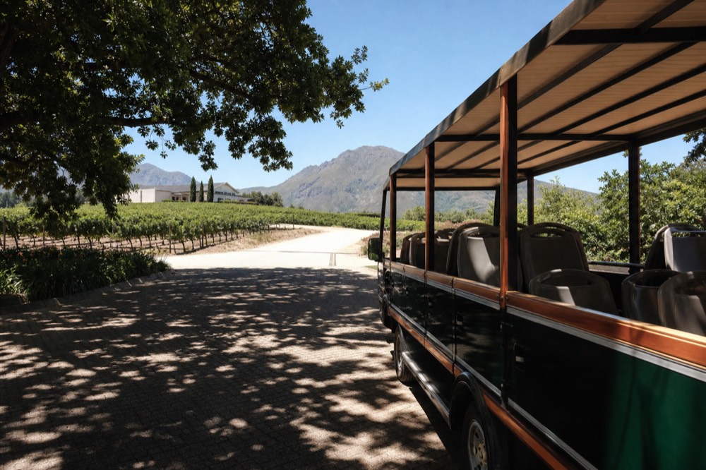 Open-air tram-bus parked at a Franschhoek wine estate entrance, no text, no logos, no people